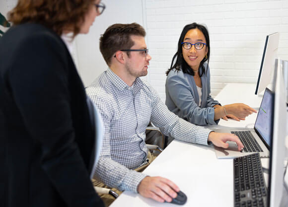 a woman pointing to a laptop screen talking to a man and another woman